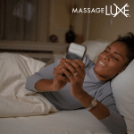 Woman lying in bed, scrolling on her phone in a dimly lit room, appearing tense and distracted.