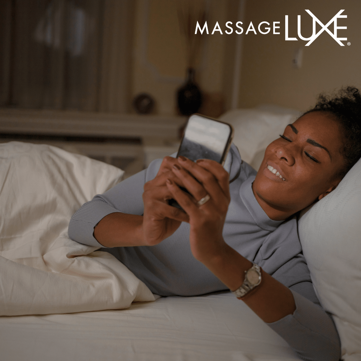 Woman lying in bed, scrolling on her phone in a dimly lit room, appearing tense and distracted.