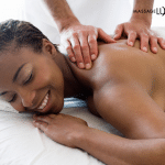 Woman smiling while receiving a back and shoulder massage from a massage therapist.